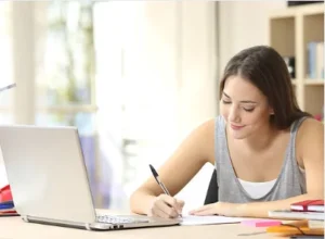 student writing scholarship essay application laptop desk university 2026
